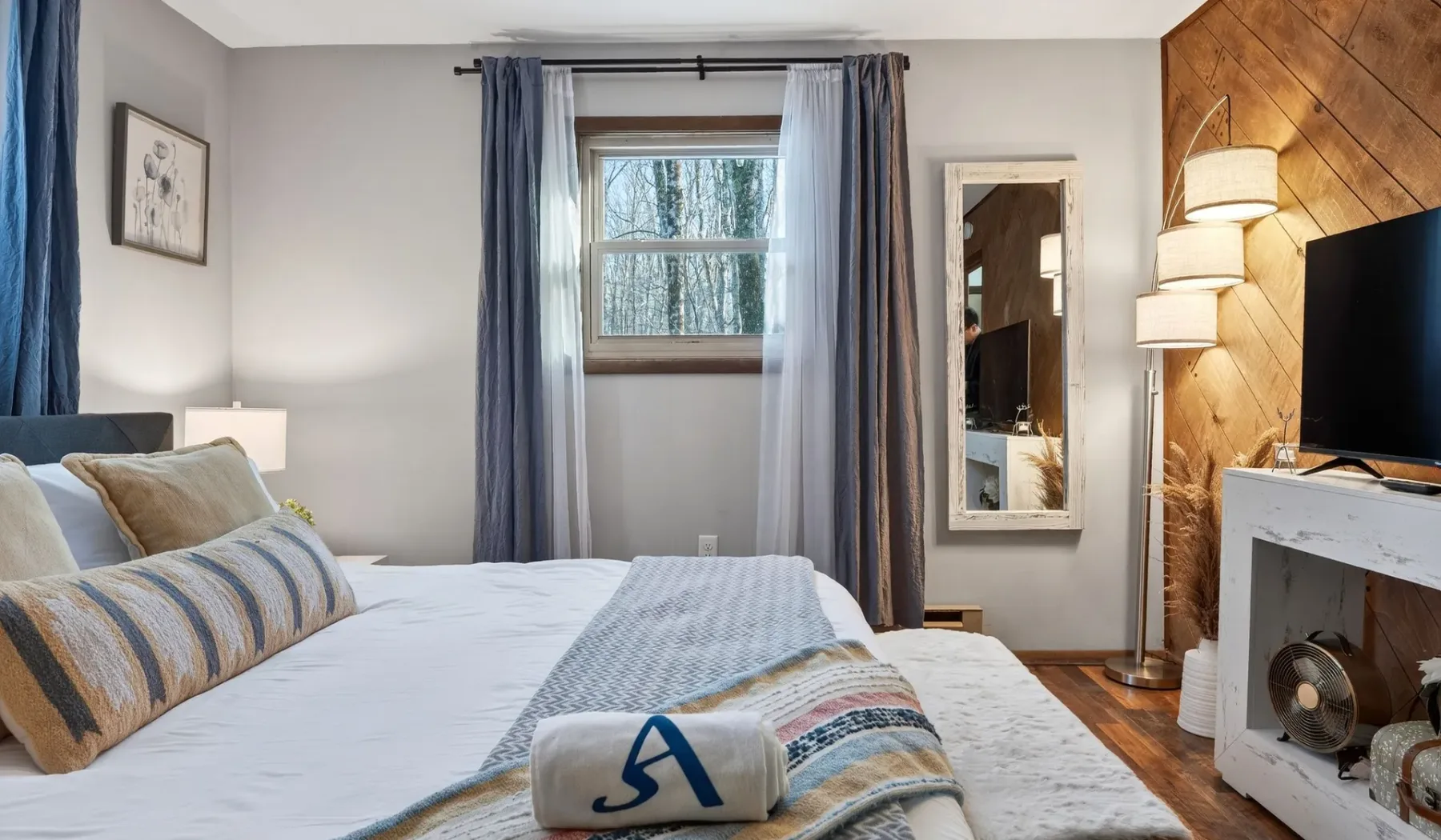 A bedroom with a neatly made bed, blue curtains, and a window.