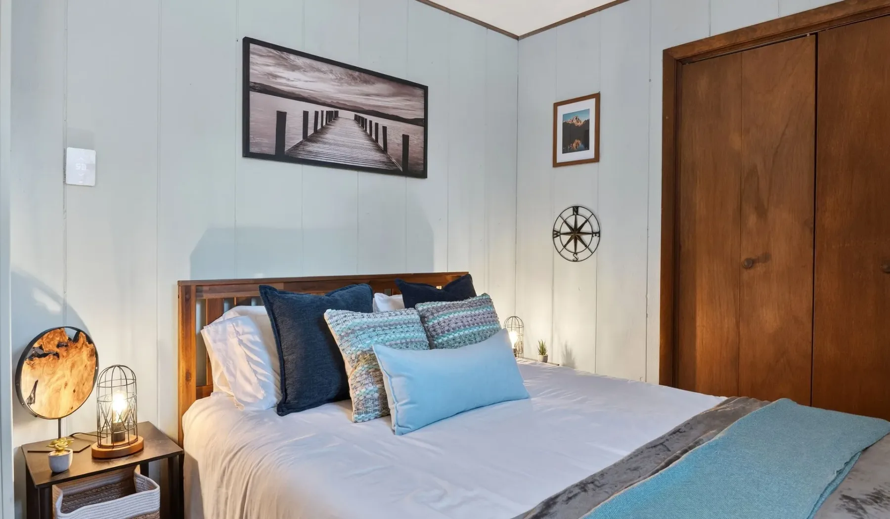 A bedroom with a bed dressed in white bedding and blue accent pillows.