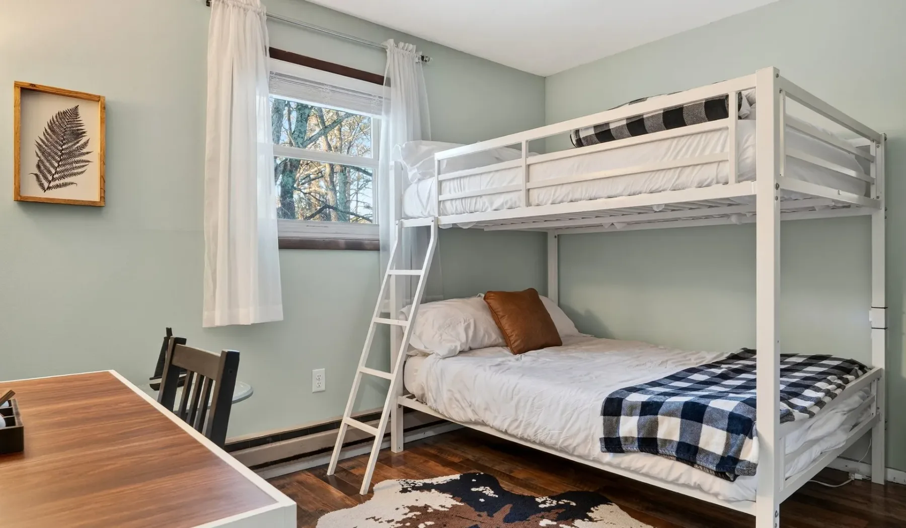 A bedroom with a white bunk bed, a desk, and a window.