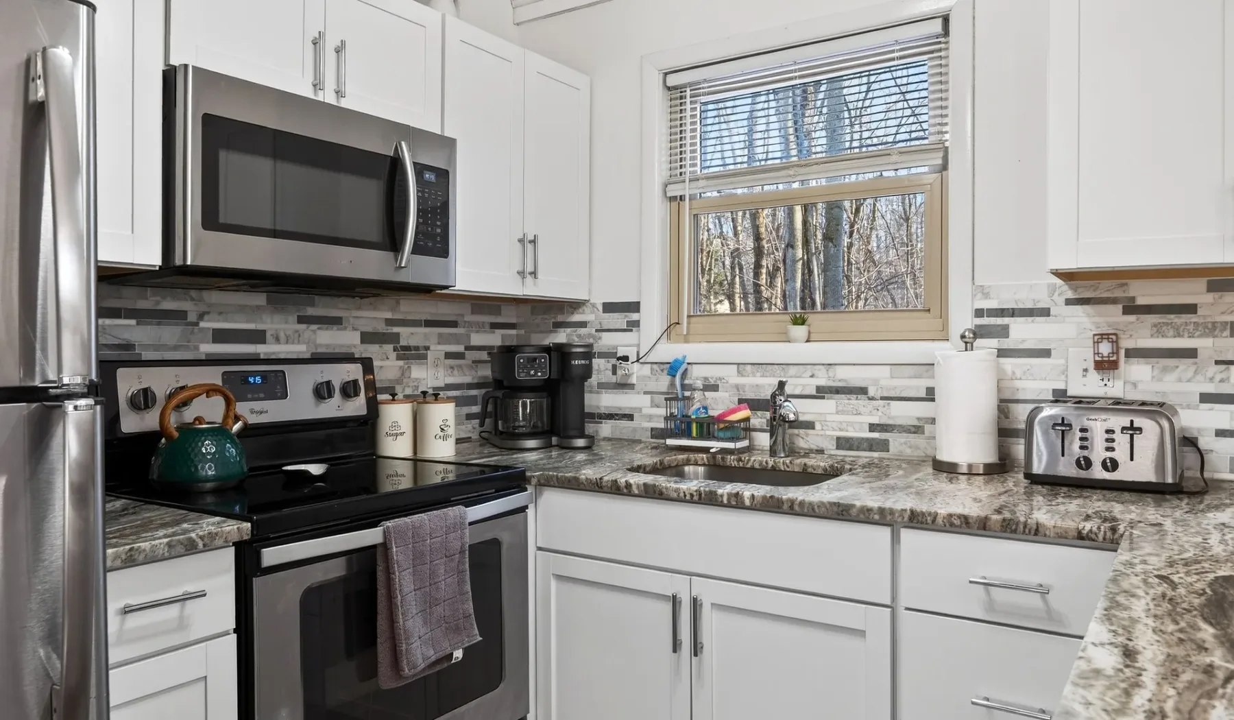 A bright kitchen with white cabinetry, dark countertops, and a window above the sink.