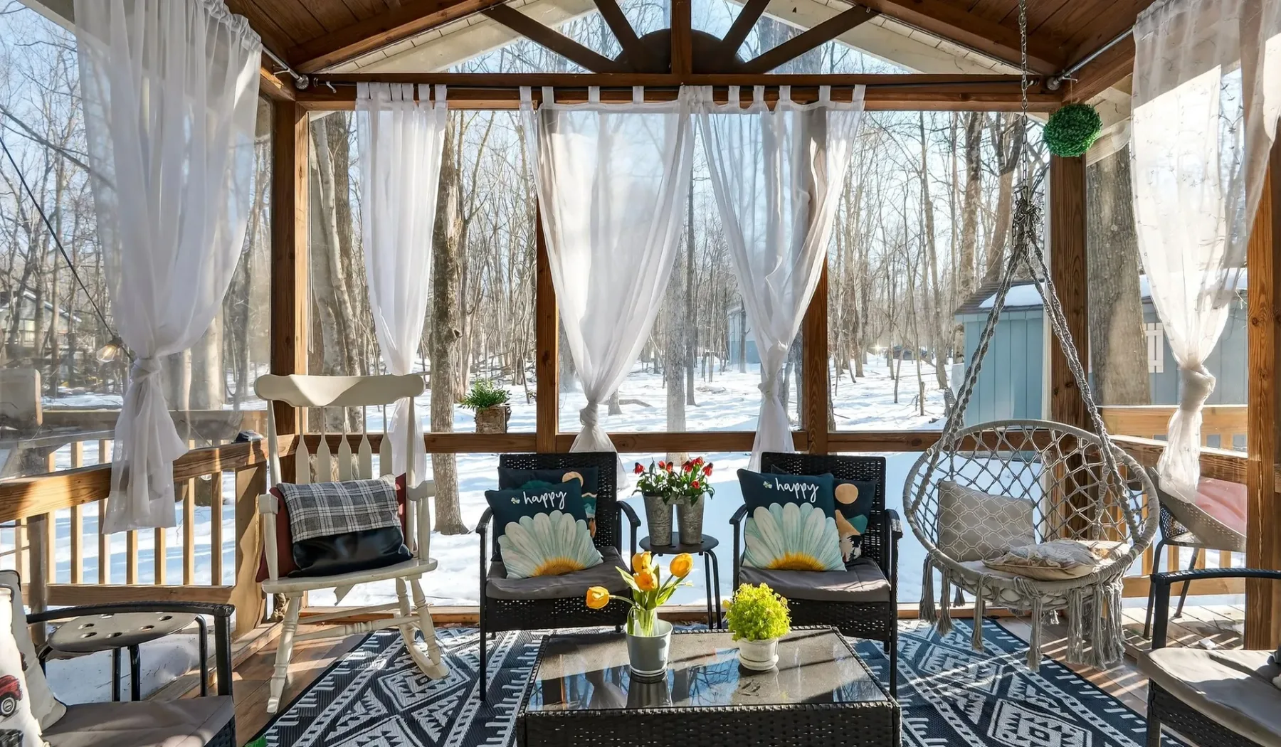 A covered outdoor seating area with curtains and views of the surrounding trees.