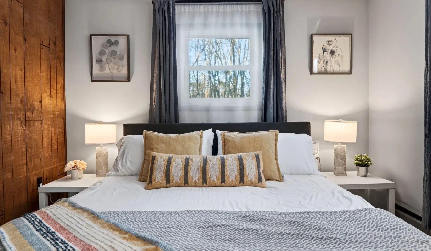 A bedroom with a neatly made bed and a window framed by dark curtains.