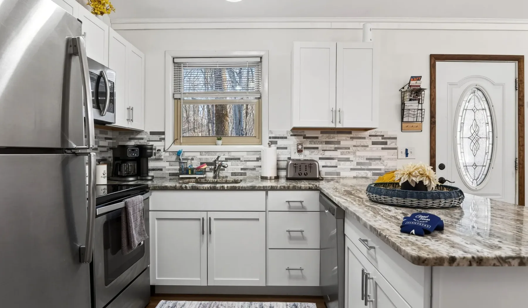 A bright kitchen with white cabinets, stainless steel appliances, and a marble-patterned counter.