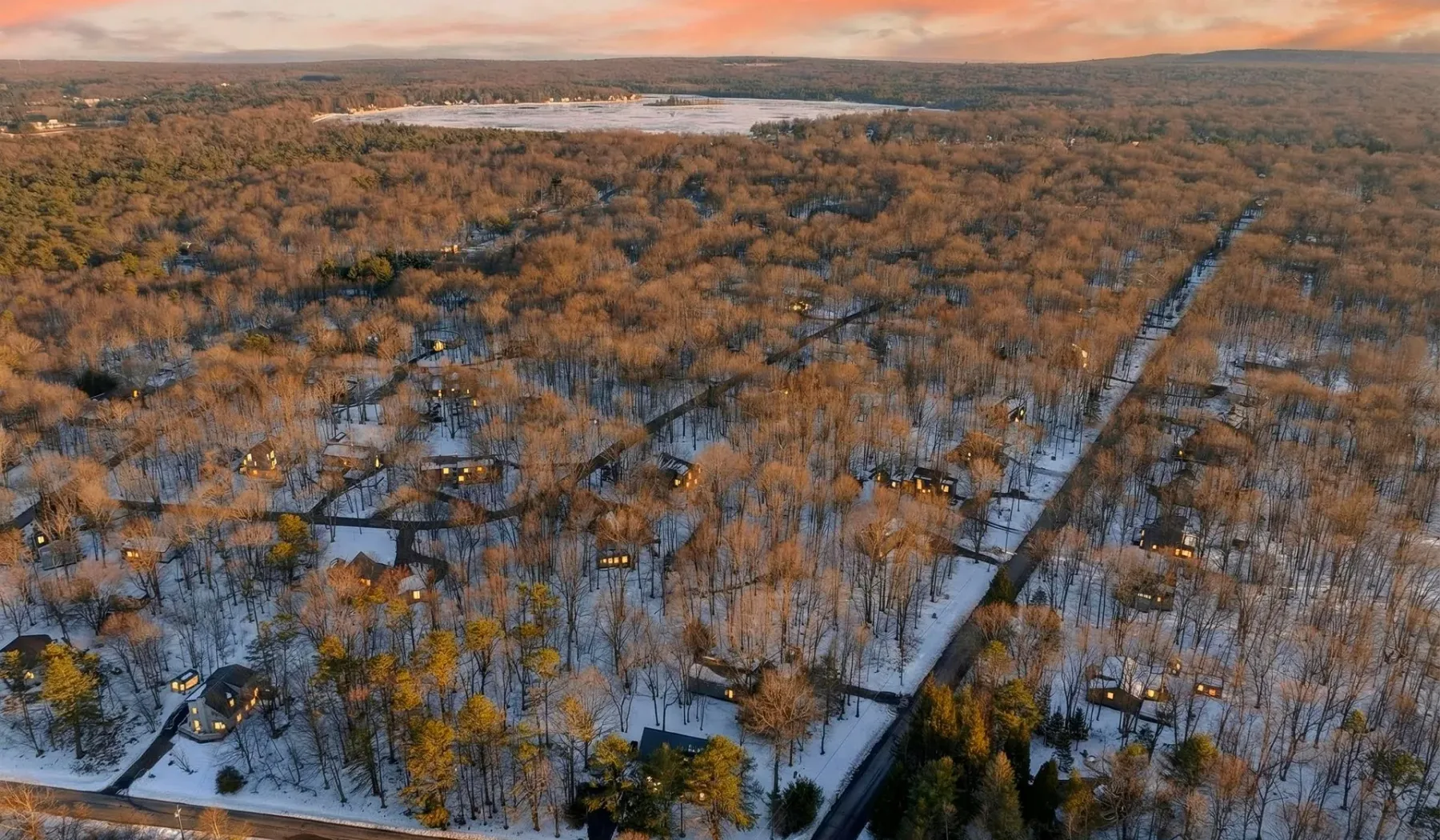 Aerial view of a wooded landscape with scattered homes and snow-covered roads.