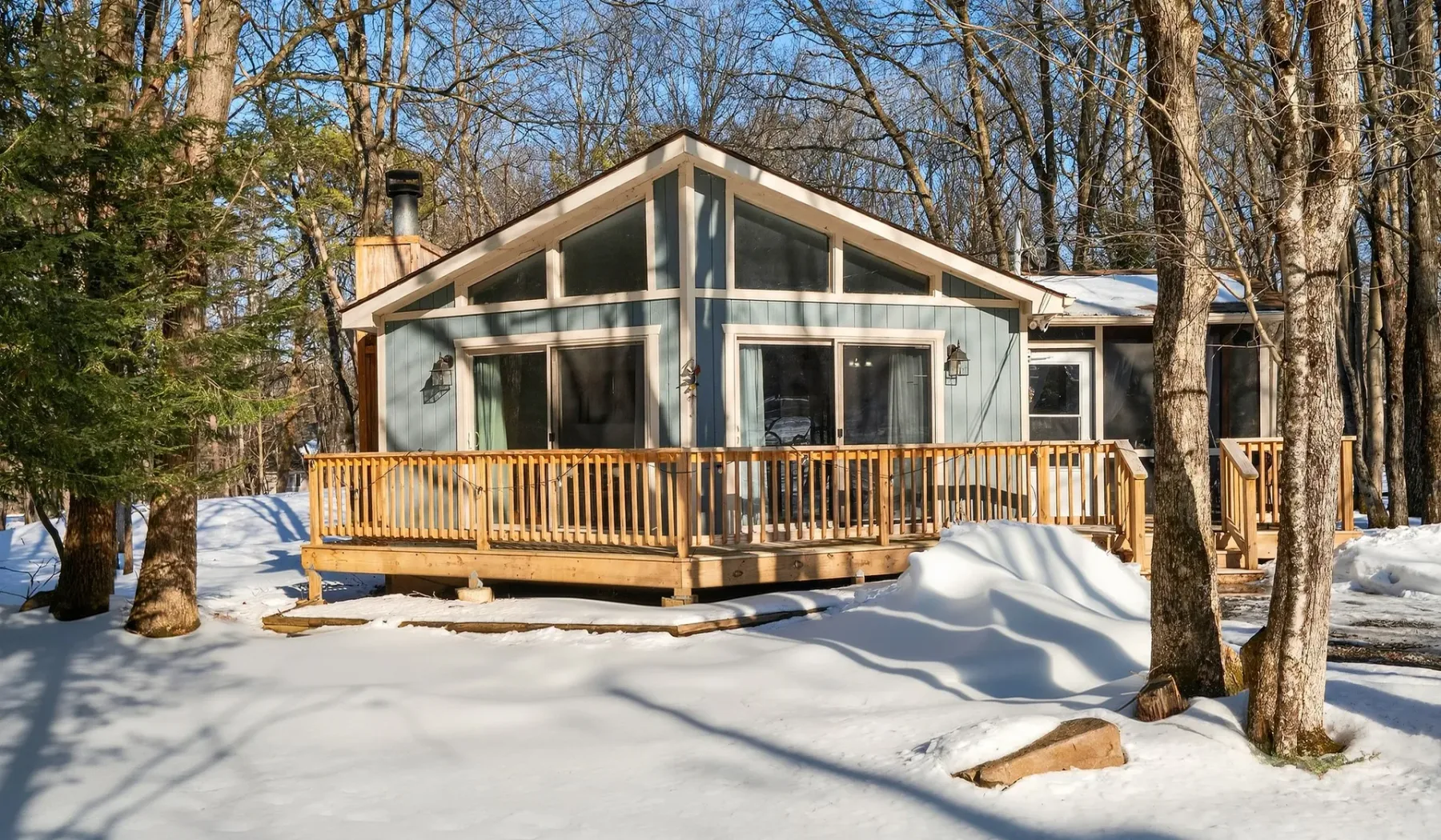 A cabin with a wooden deck sits among trees in a snowy landscape.