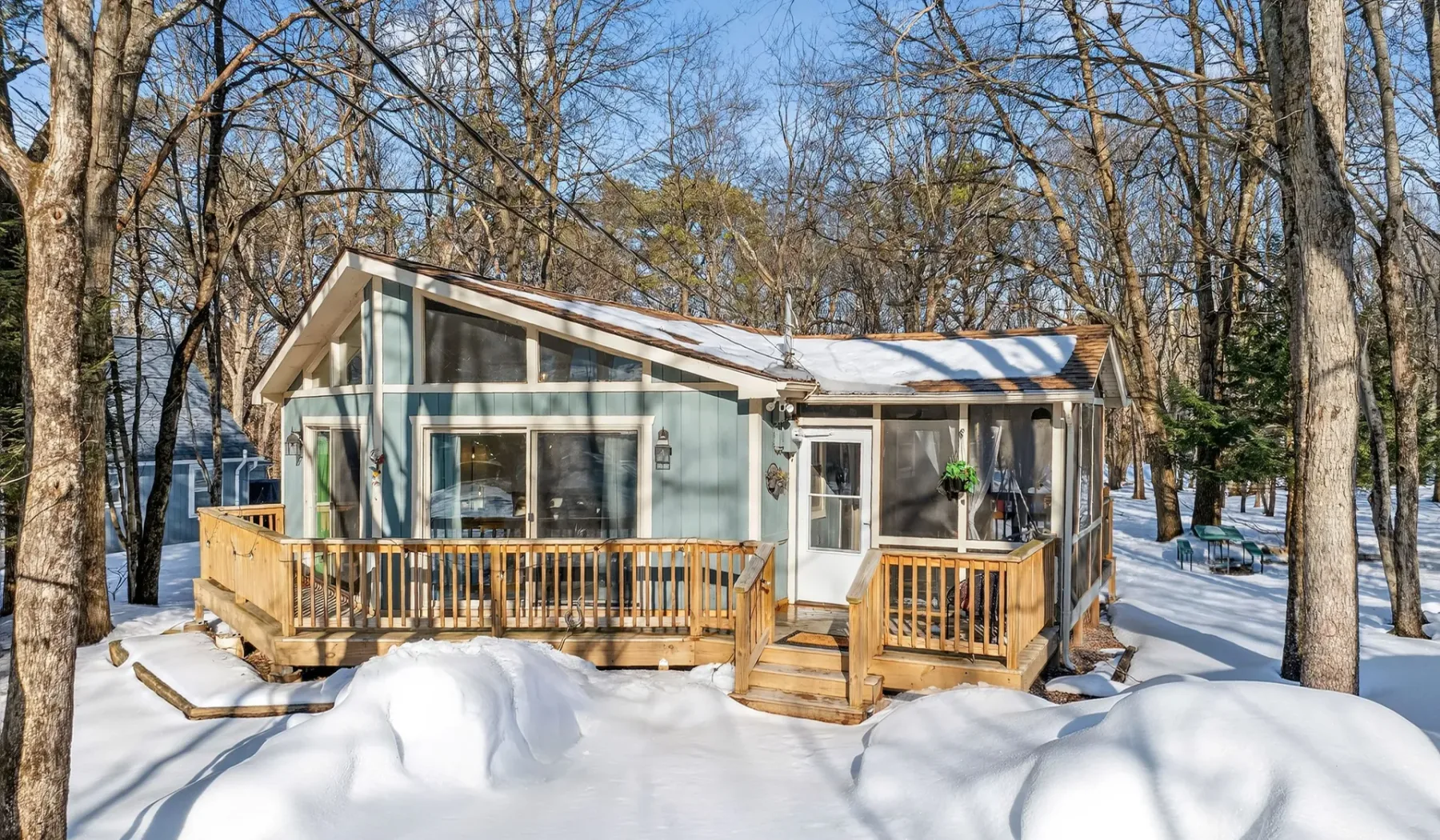 A small cabin with a wooden deck sits among snow-covered trees.