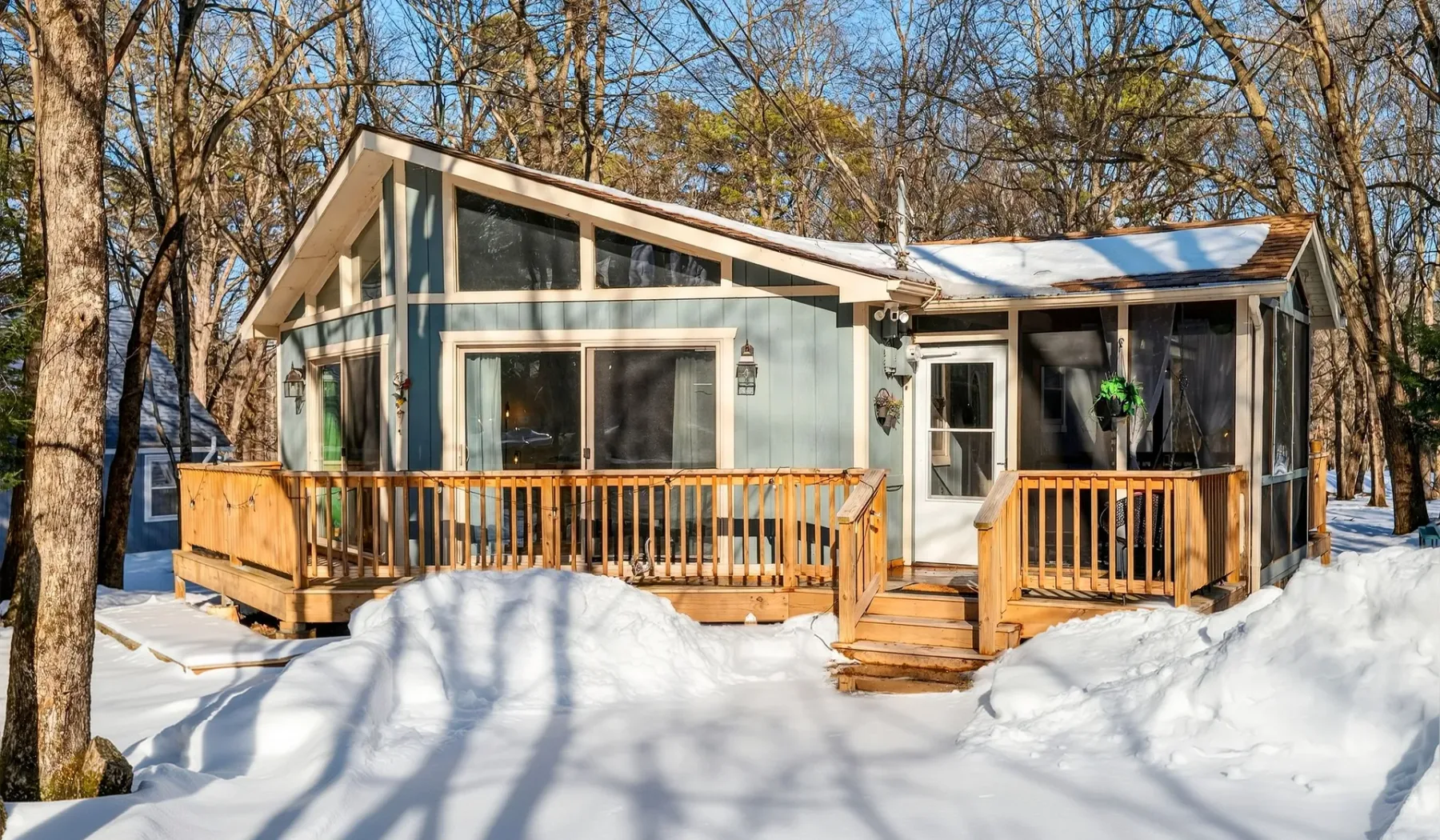 A cabin with a wooden deck sits among snow-covered trees.