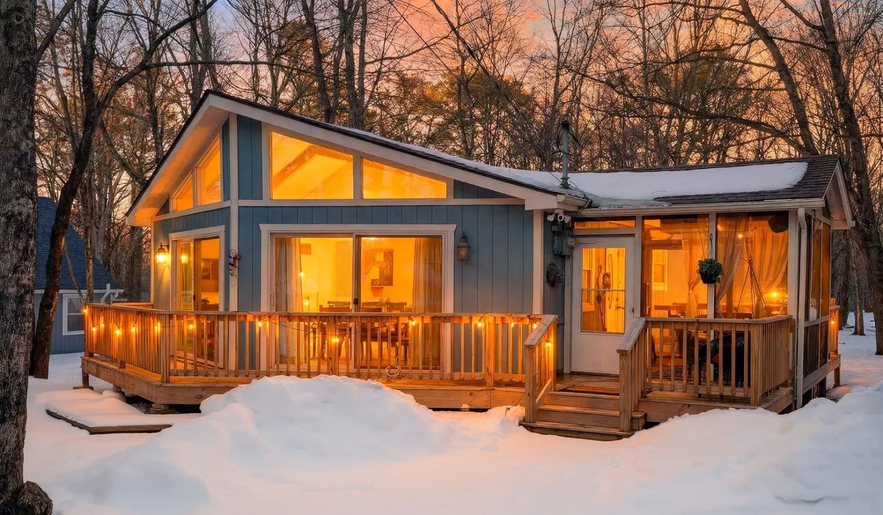 A modern cabin glows warmly among snow-covered trees at dusk.