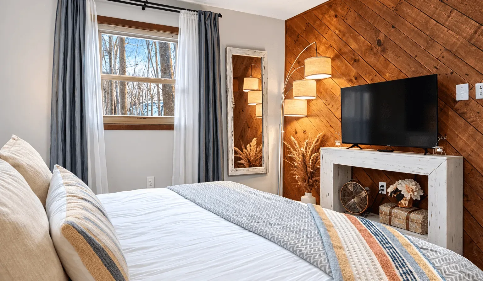 A bedroom with a neatly made bed, a television, and warm wood paneling.
