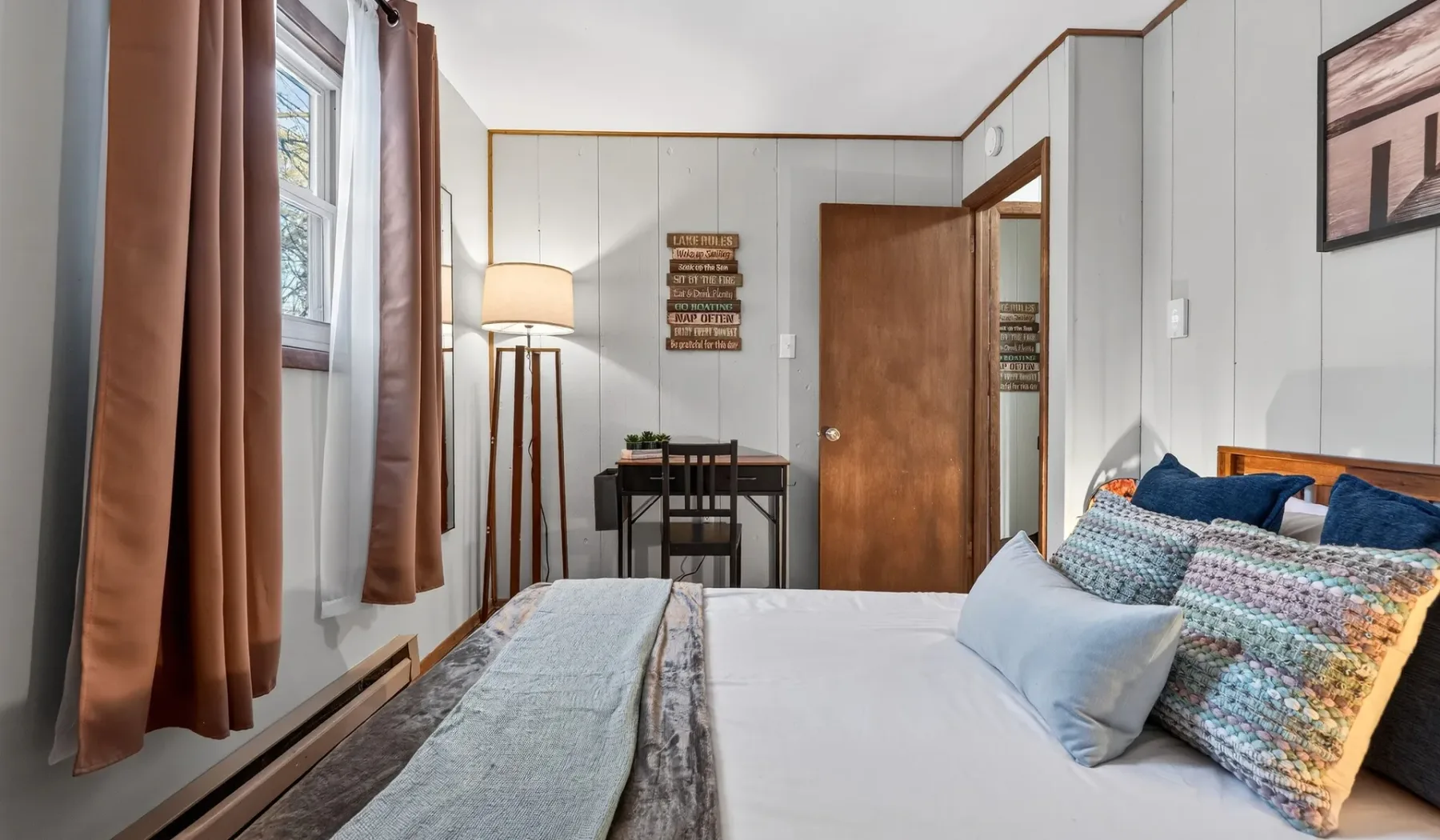 A bedroom with a neatly made bed, curtained windows, and a small dining table.