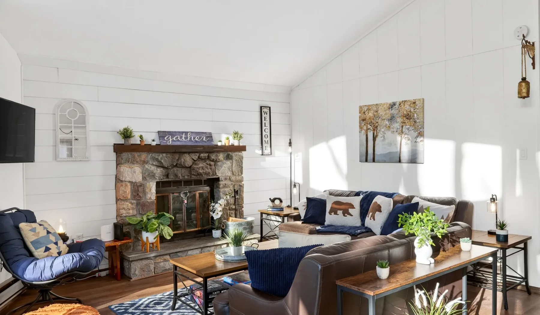 A bright living room with seating arranged around a stone fireplace.