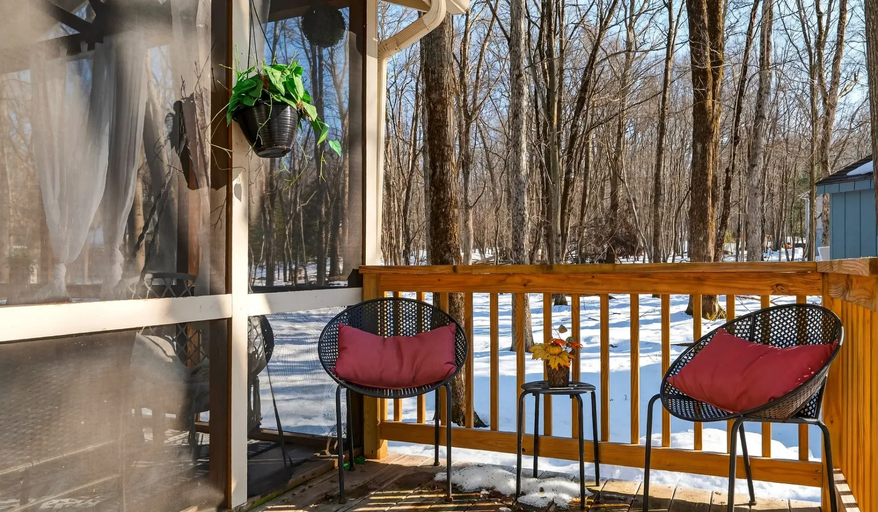 A small outdoor deck with seating and a wooden railing overlooks a snowy wooded area.