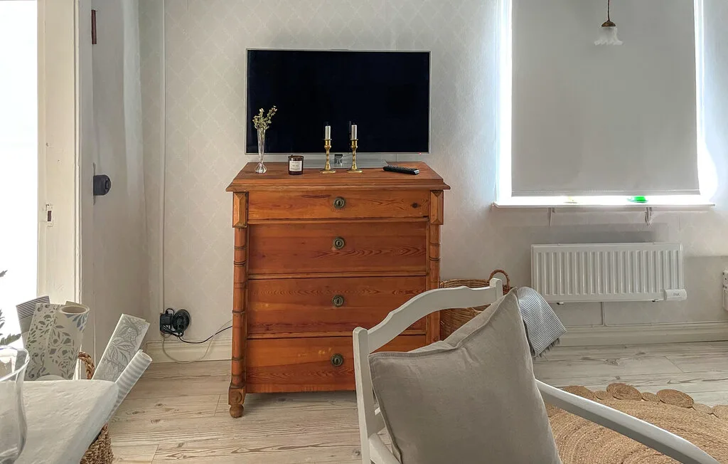 Una zona de estar en un dormitorio con una cómoda de madera bajo un televisor de pared.