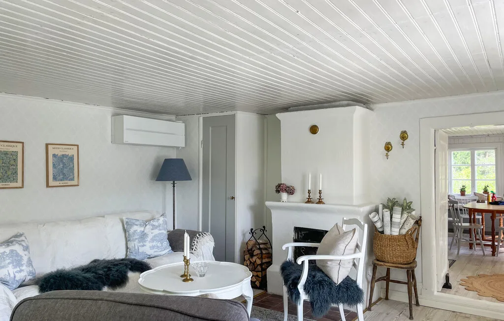 Una sala luminosa con asientos blancos, una mesa redonda y una puerta abierta hacia el comedor.