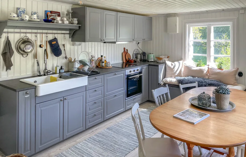 Una luminosa cocina con comedor, gabinetes grises y una mesa de madera.