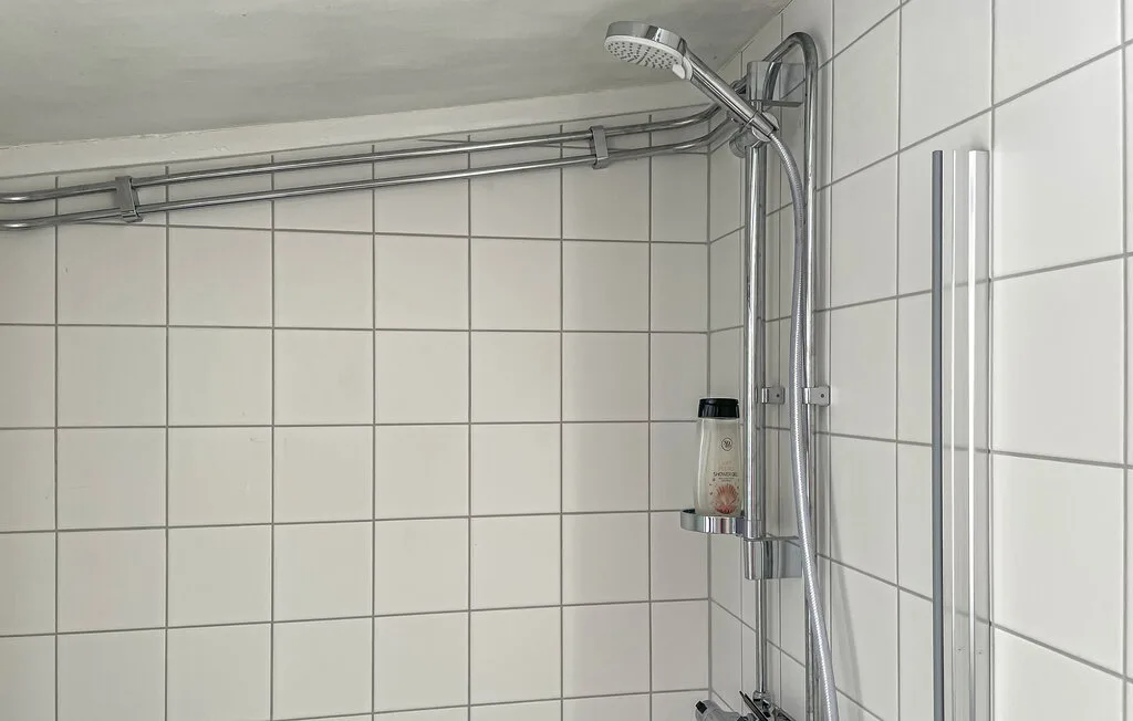Una zona de ducha alicatada con ducha de mano y accesorios.