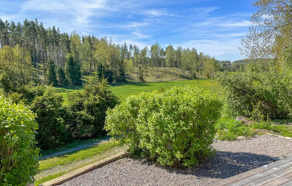 Un patio de grava junto a arbustos verdes, con un paisaje boscoso al fondo.