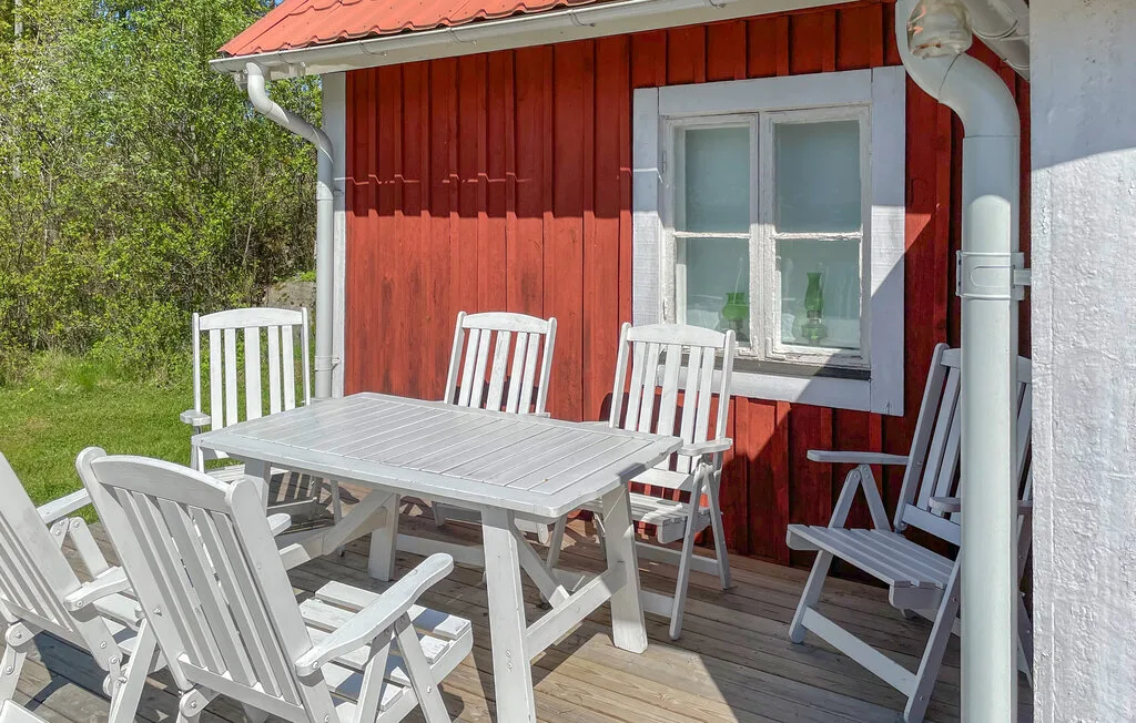 Un patio de madera con una mesa de comedor blanca y asientos junto a una pared roja.