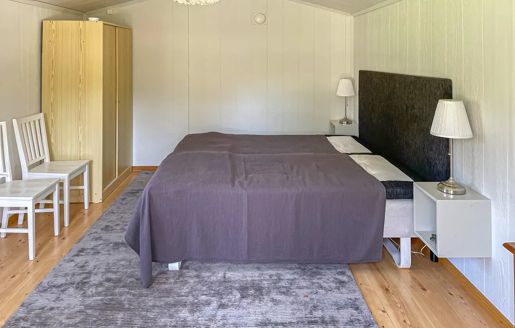 Un dormitorio con una cama cubierta con una manta oscura y una alfombra gris.