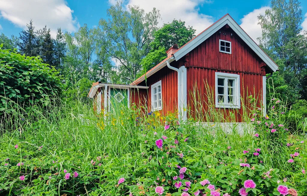 Una casa roja de madera está rodeada de hierbas altas y flores rosadas.