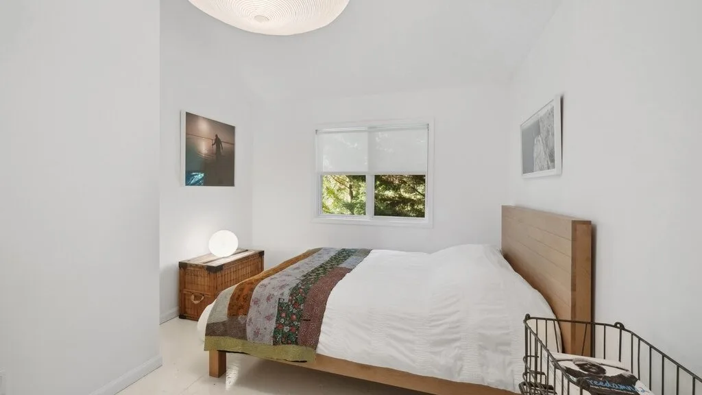 Un dormitorio luminoso con cama, mesita de noche y ventana.