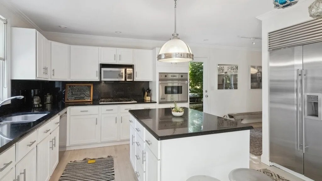 Una cocina luminosa con armarios blancos y una isla central con encimera oscura.