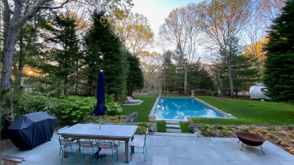 Una piscina al aire libre está junto a un patio pavimentado y árboles.
