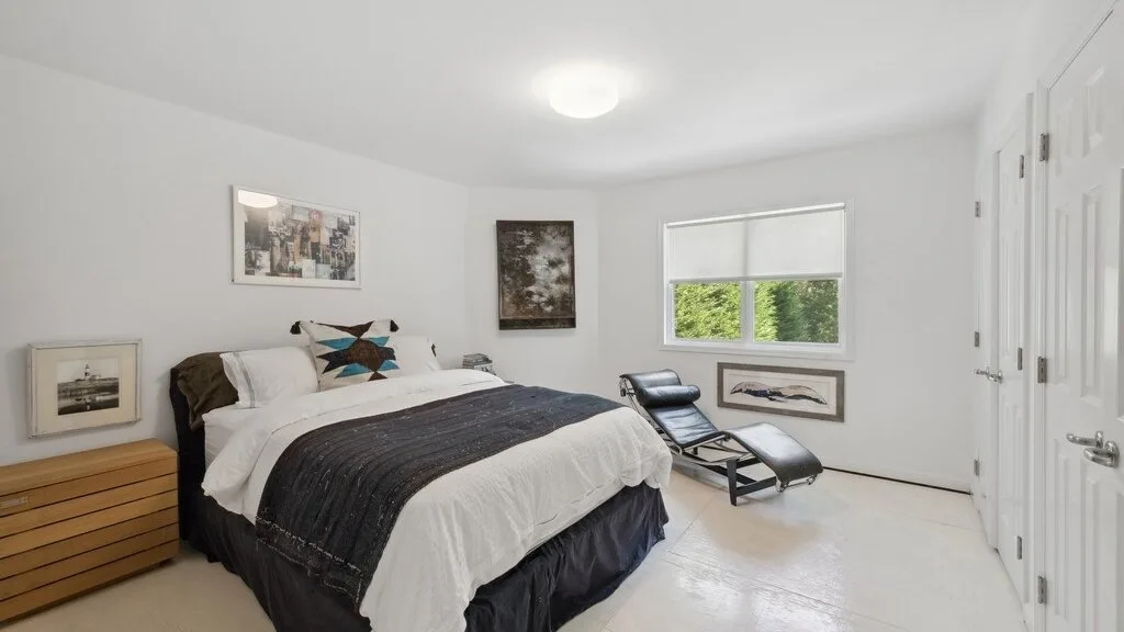 Un dormitorio luminoso con una cama y una silla de descanso junto a la ventana.