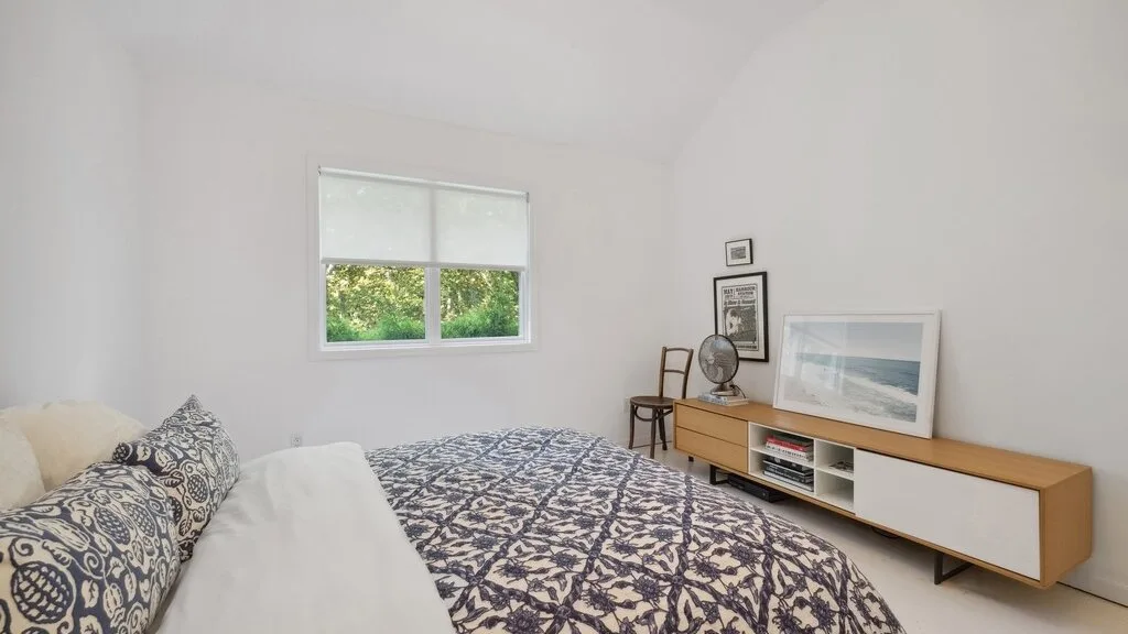 Un dormitorio luminoso con una colcha estampada y una ventana con vista a la vegetación.