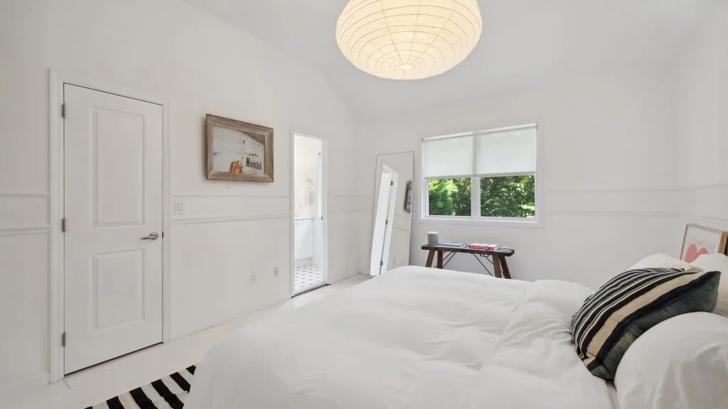 Un dormitorio luminoso con una cama bien tendida y una ventana con vistas a la vegetación.