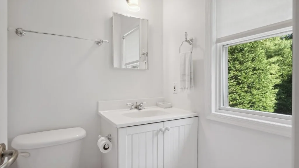 Un baño luminoso con lavabo, inodoro y una ventana con vista a la vegetación.