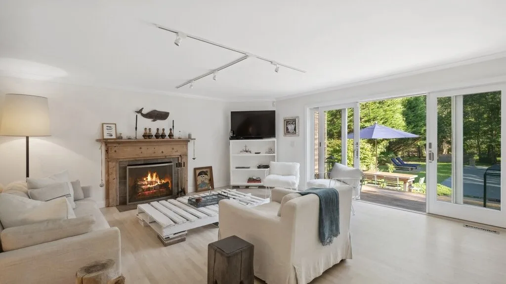Una sala de estar luminosa con asientos, una chimenea y grandes ventanas hacia la vegetación.