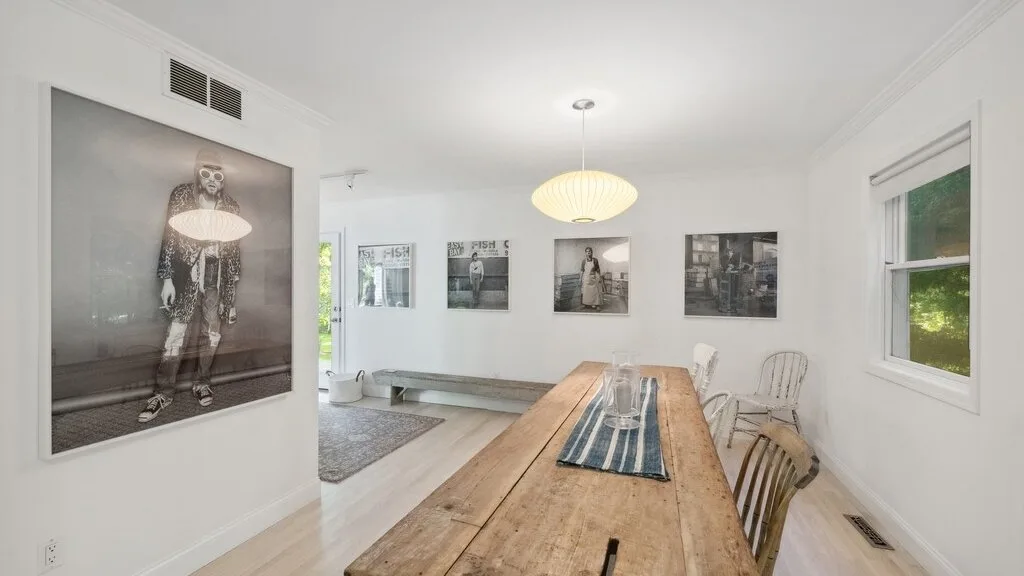 Un comedor luminoso con una mesa larga de madera y cuadros enmarcados.