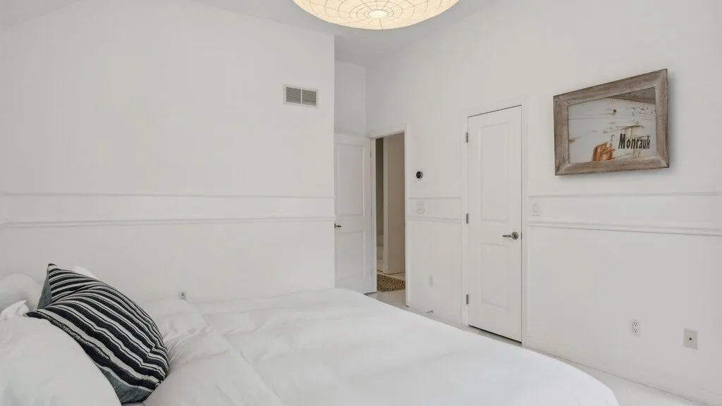 Un dormitorio luminoso con ropa de cama blanca y un cojín a rayas.