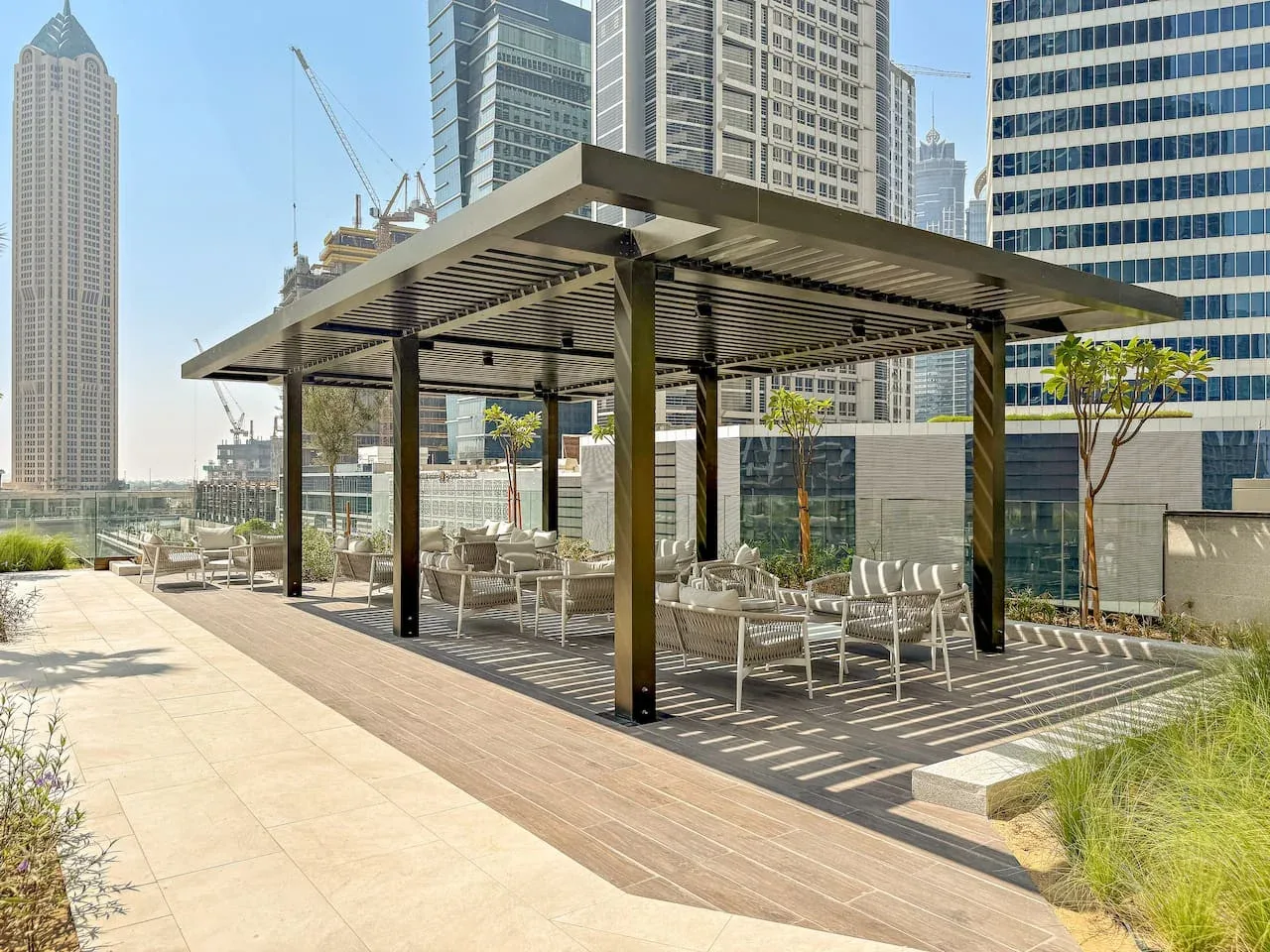 An outdoor rooftop seating area beneath a shaded pergola, with city buildings in the background.