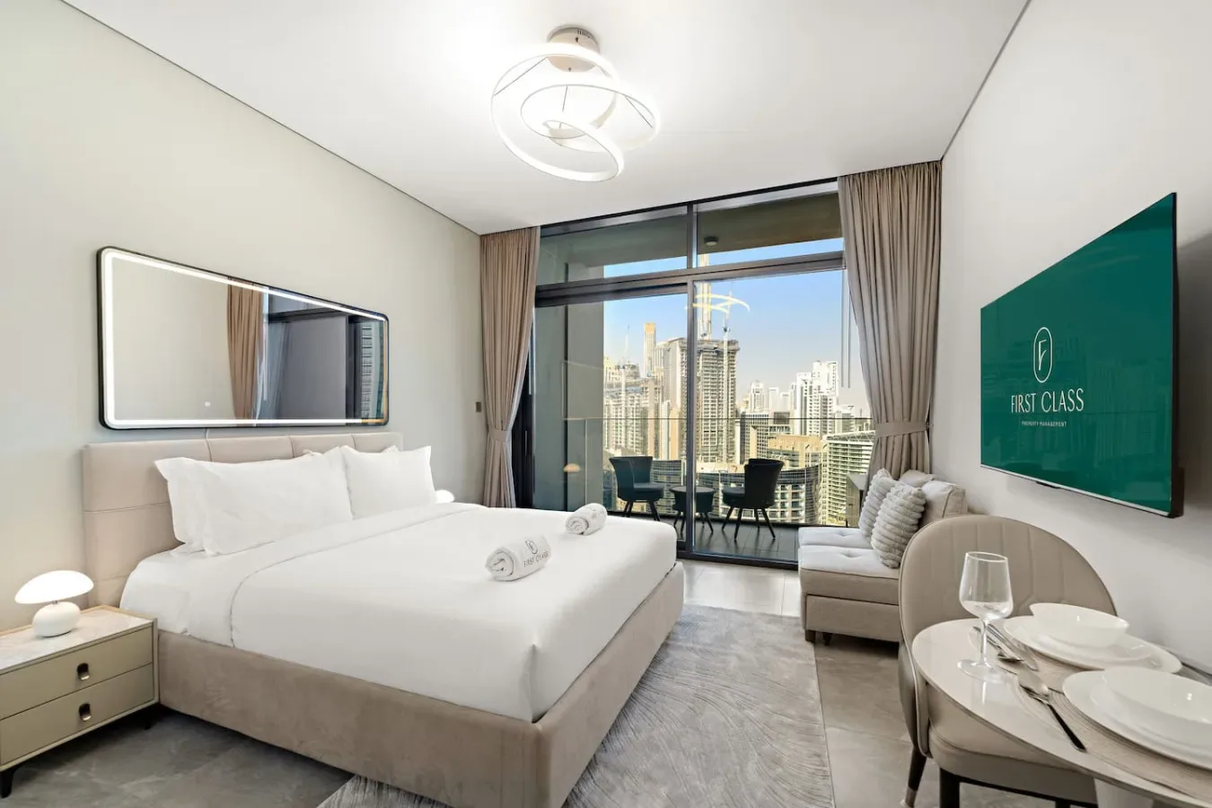 A bright bedroom with a neatly made bed beside floor-to-ceiling windows overlooking the city.