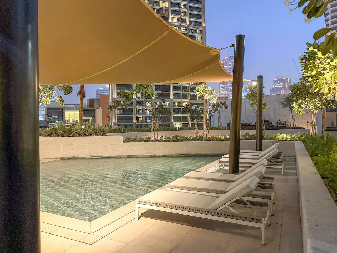 An outdoor pool beside a row of lounge chairs under a shade canopy.