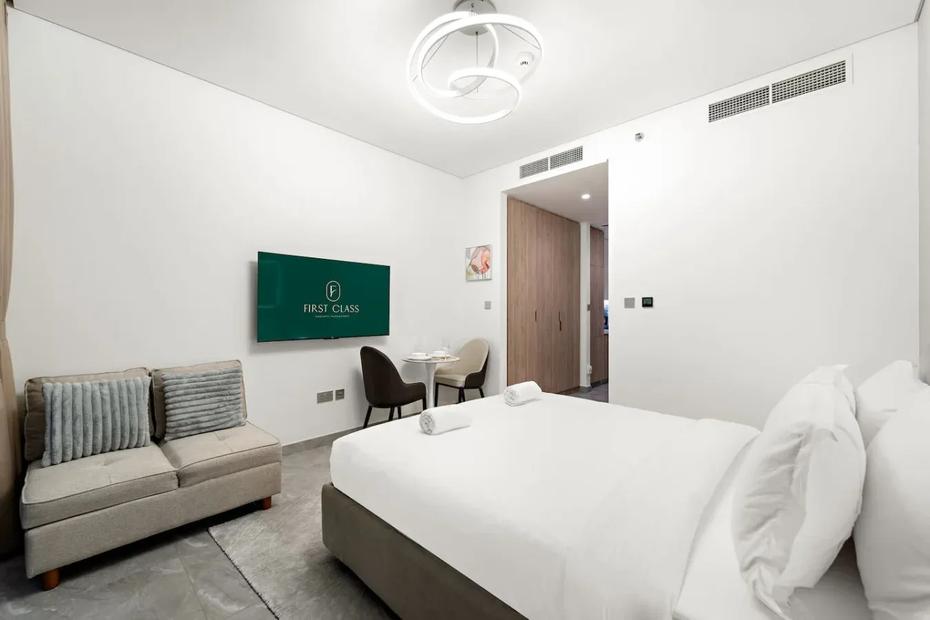 A bright bedroom with a large bed, a gray seating area, and a wooden door.