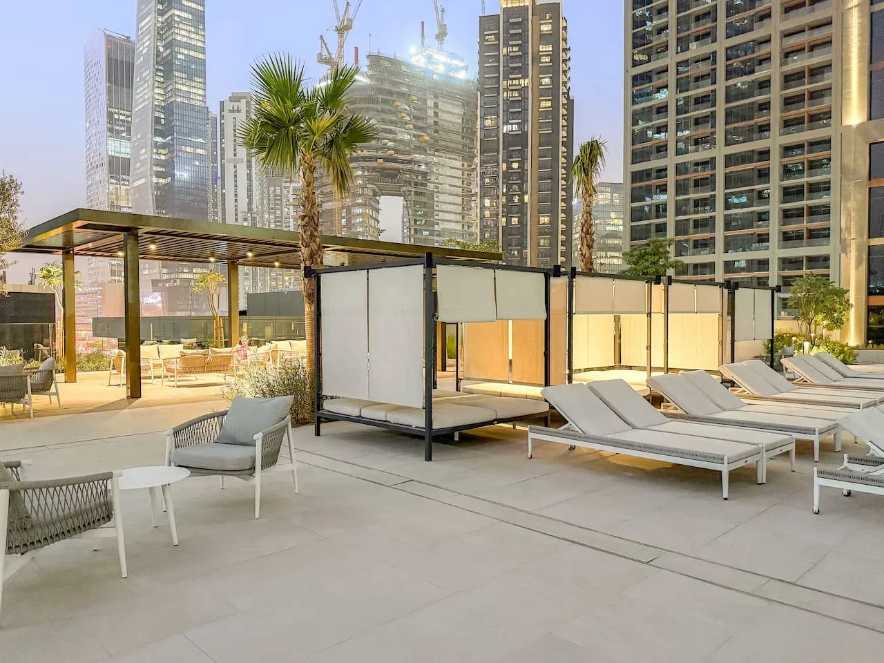 An outdoor poolside lounge area with sun loungers and tall buildings beyond.