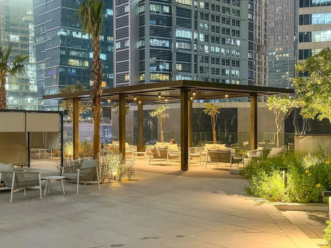 A rooftop terrace with outdoor seating and illuminated office buildings in the background.