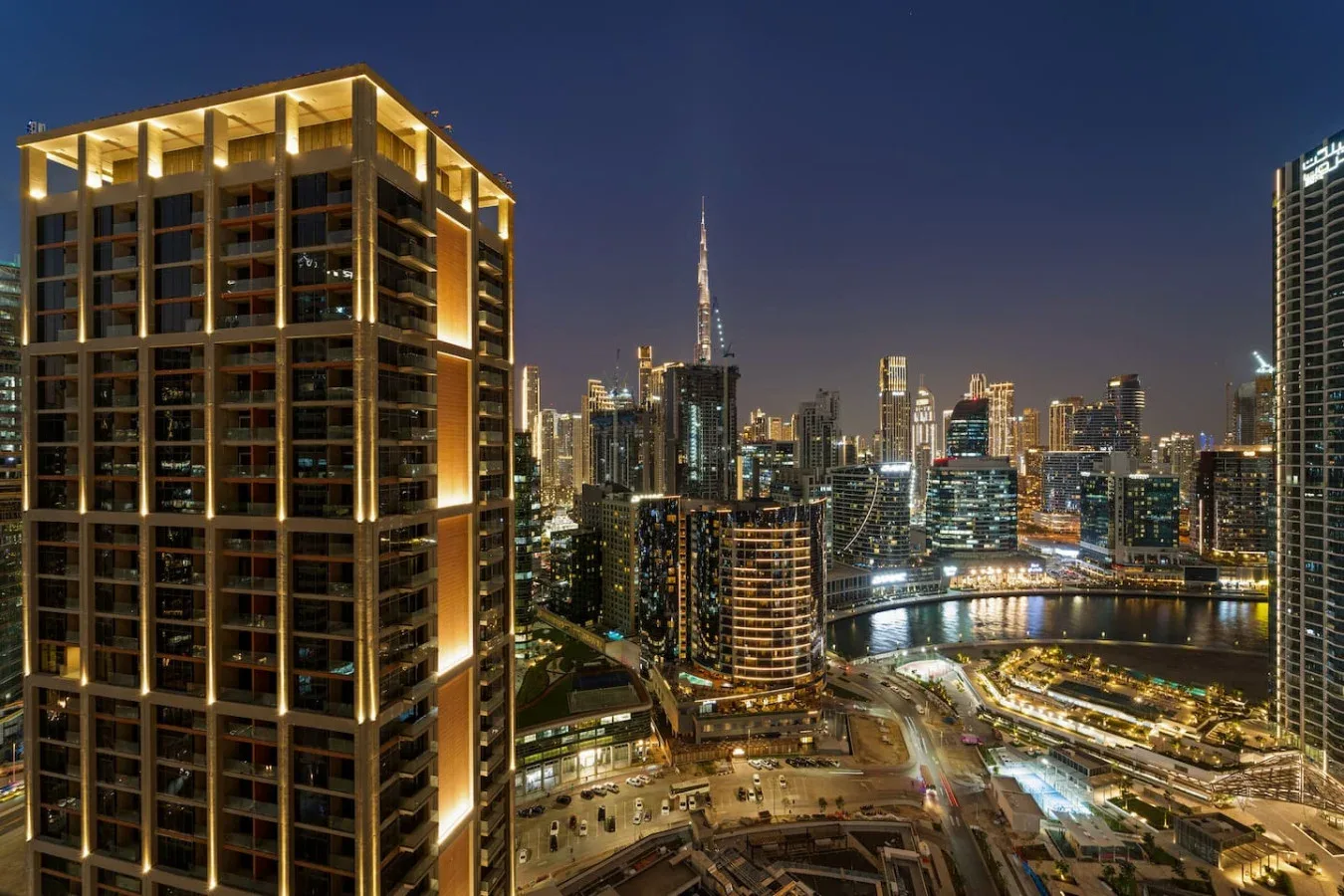 A city skyline at night overlooks a brightly lit waterfront.