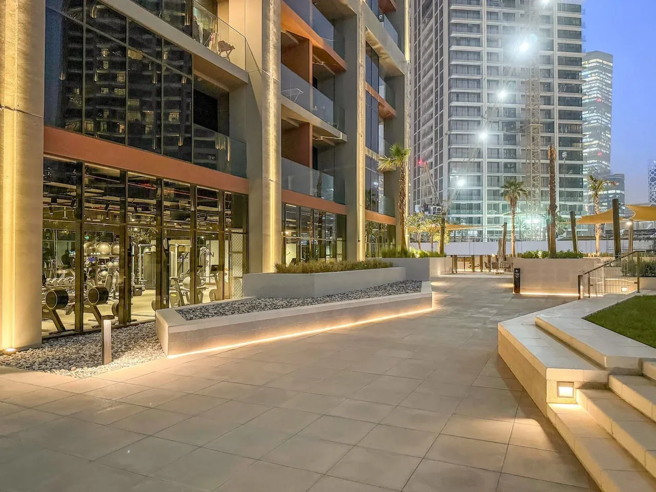 A modern building entrance opens onto a paved outdoor plaza with planters.