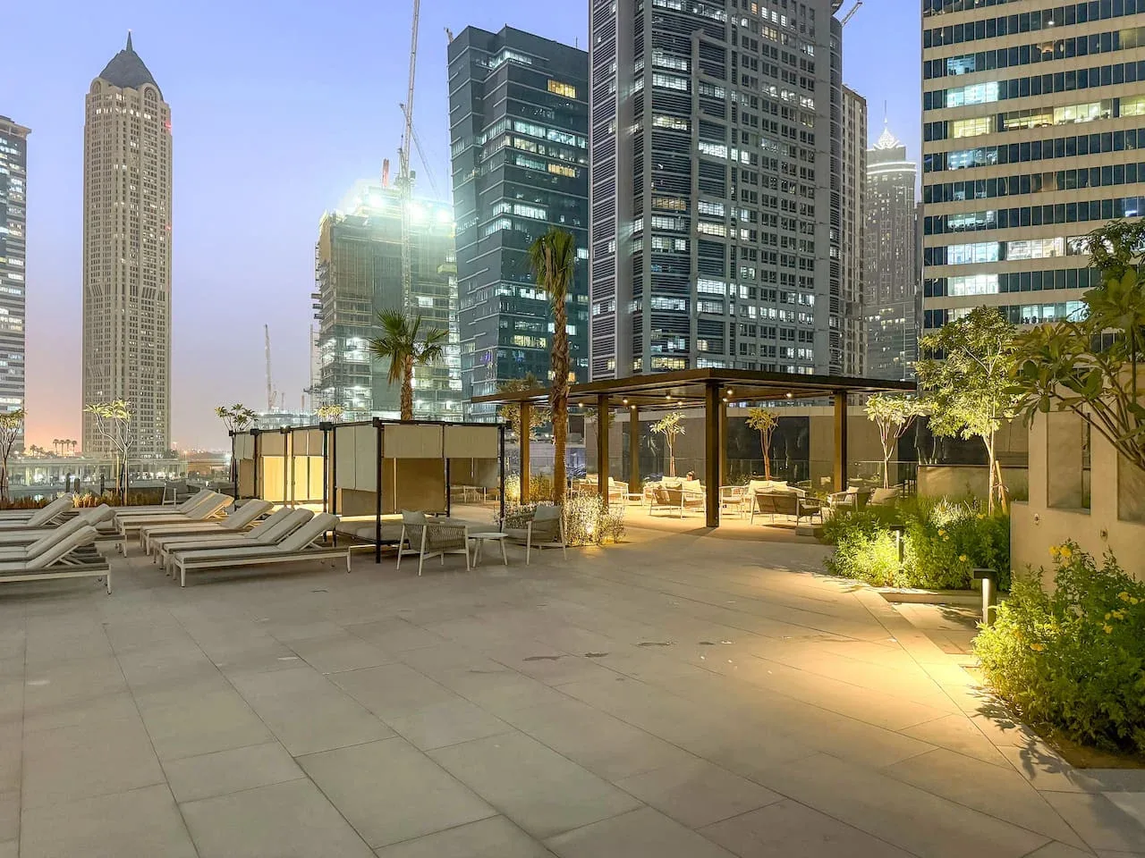A rooftop terrace with lounge seating and greenery overlooks surrounding city buildings.