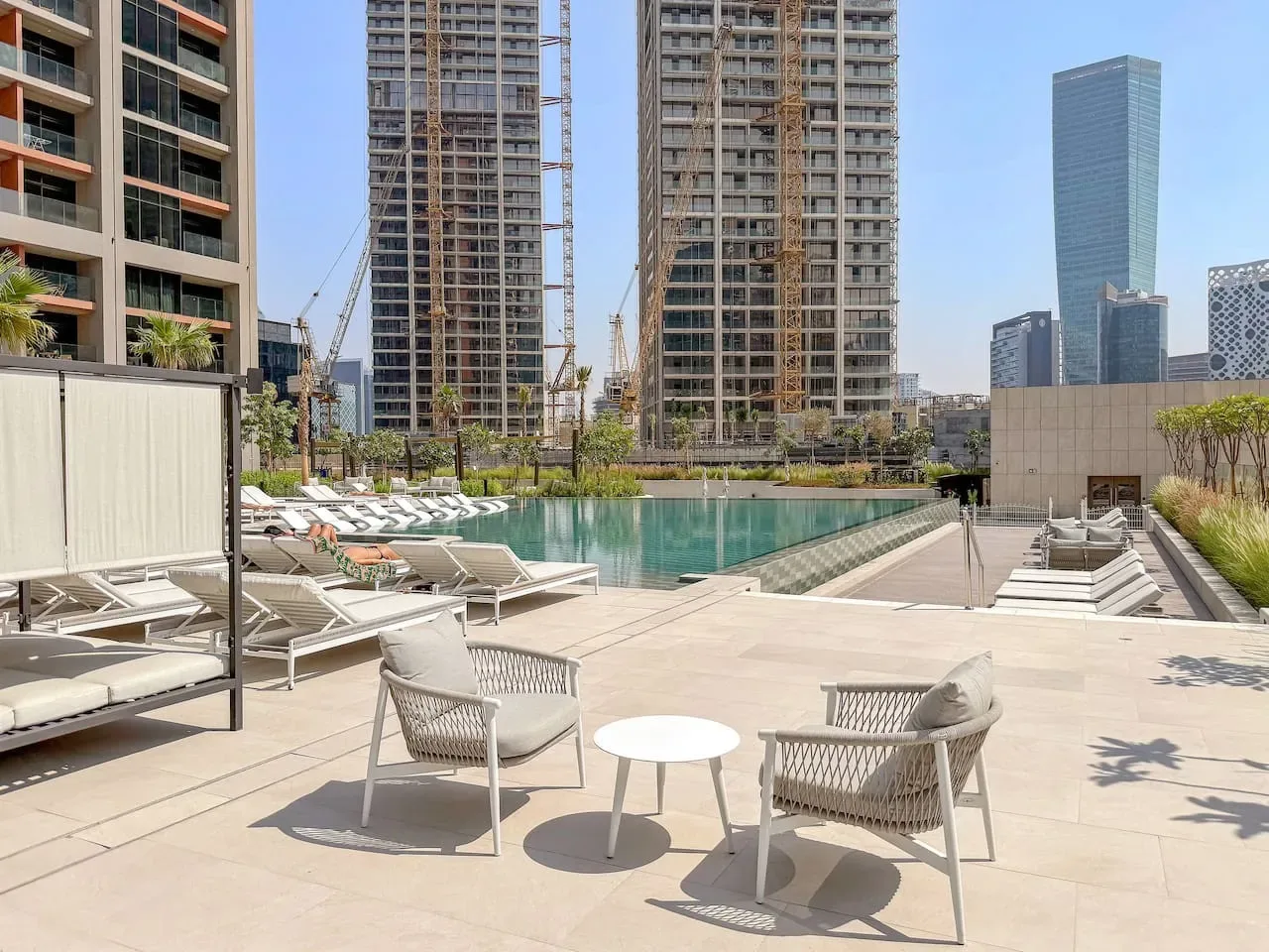 A rooftop pool and surrounding terrace with outdoor seating and city buildings beyond.