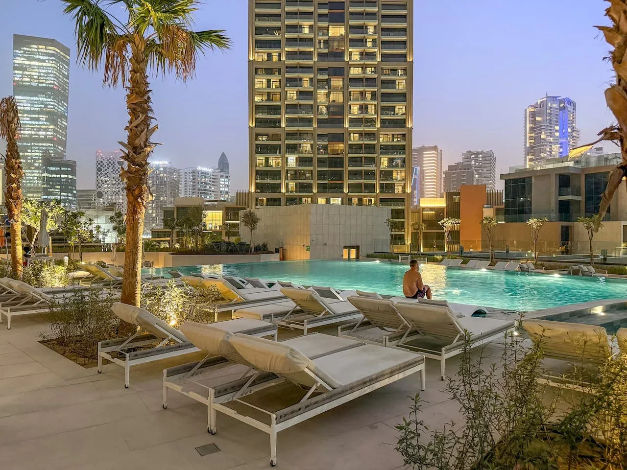 An outdoor swimming pool with lounge seating and city buildings in the background.