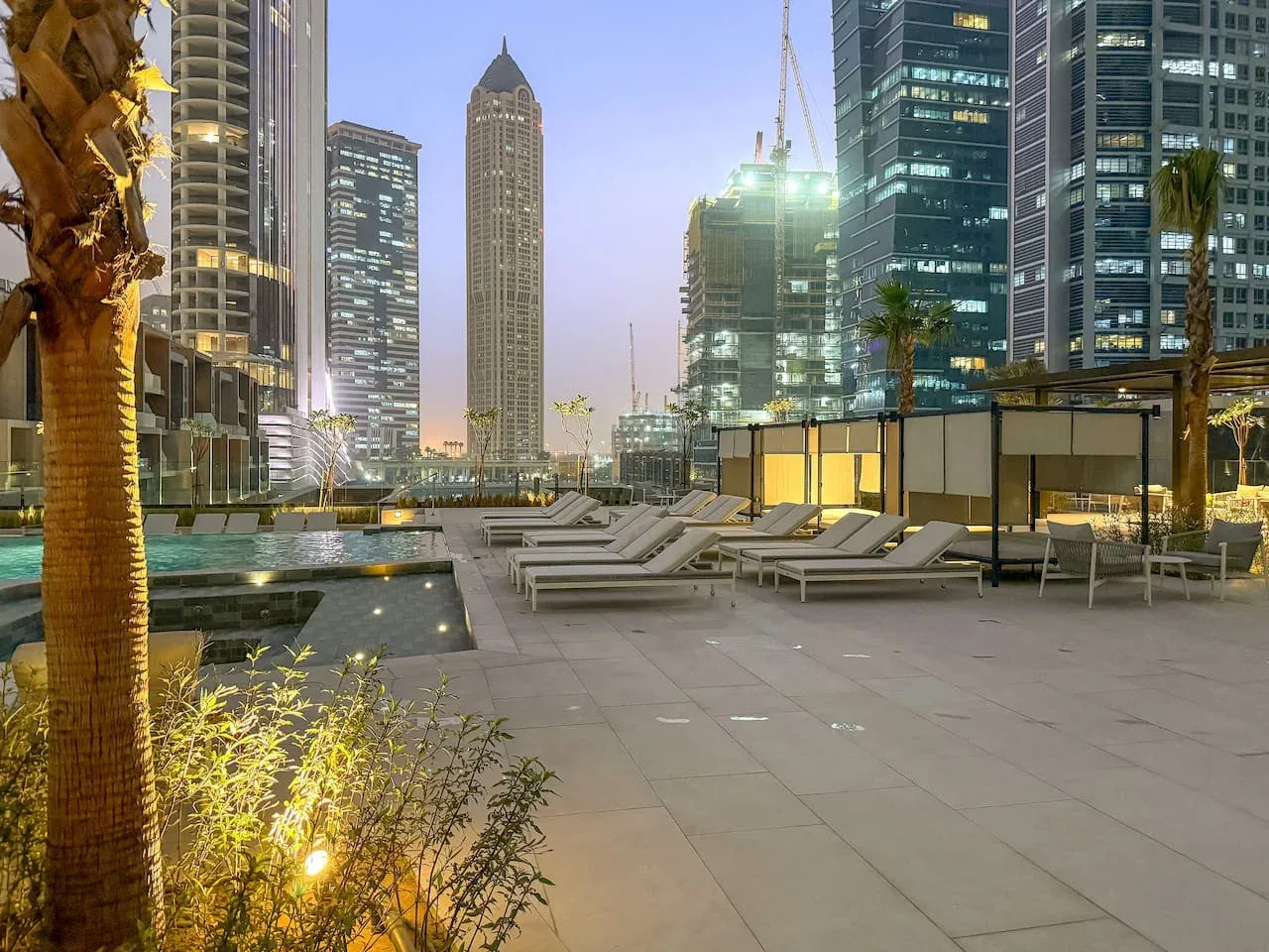 A rooftop terrace with lounge seating overlooks a city skyline at dusk.