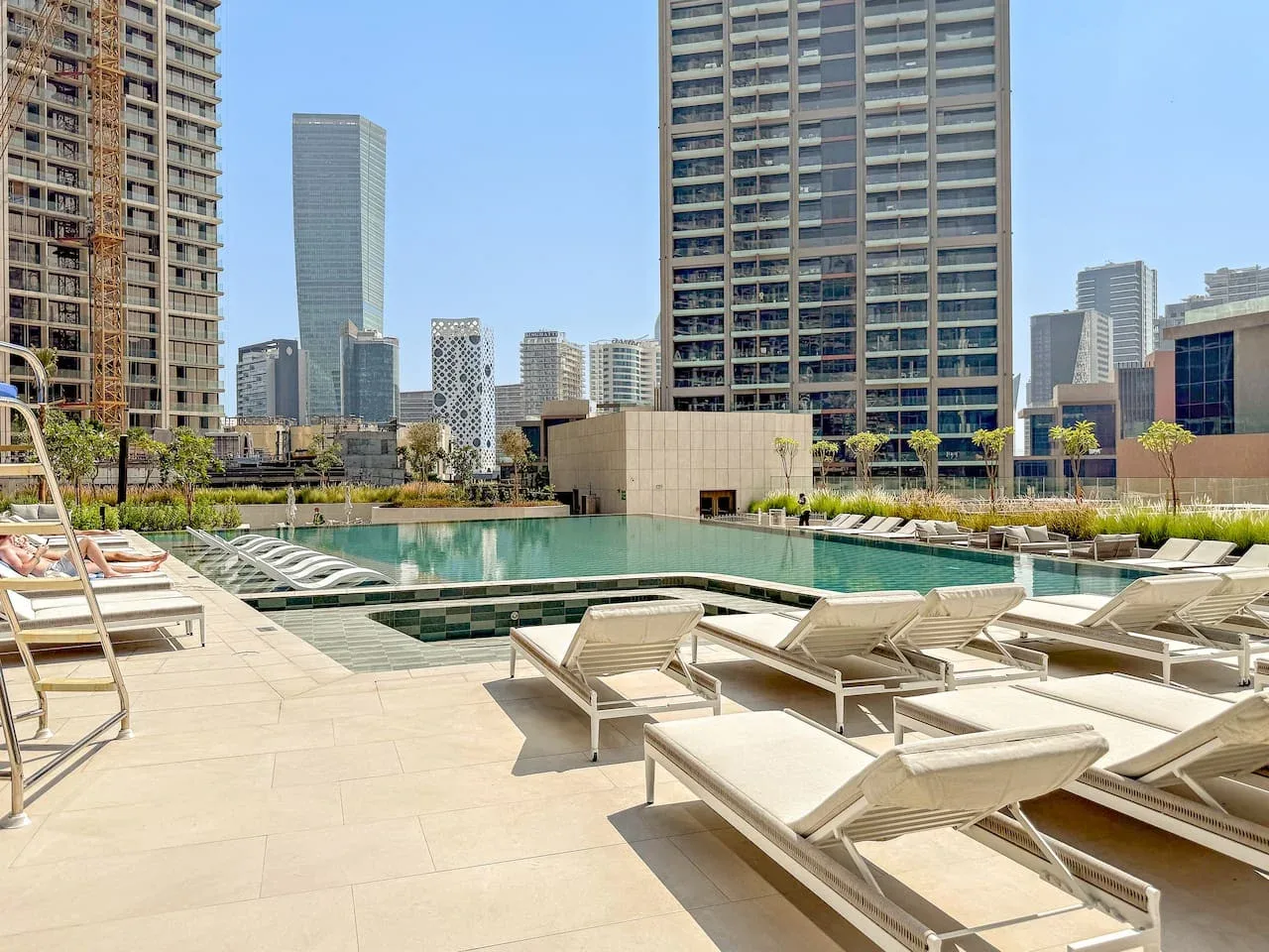 A rooftop pool area with lounge chairs and tall buildings in the background.