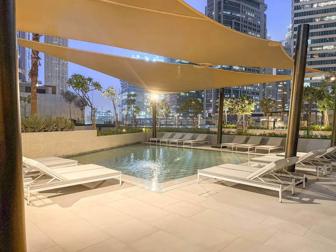 An outdoor swimming pool with lounge seating beneath broad shade canopies.