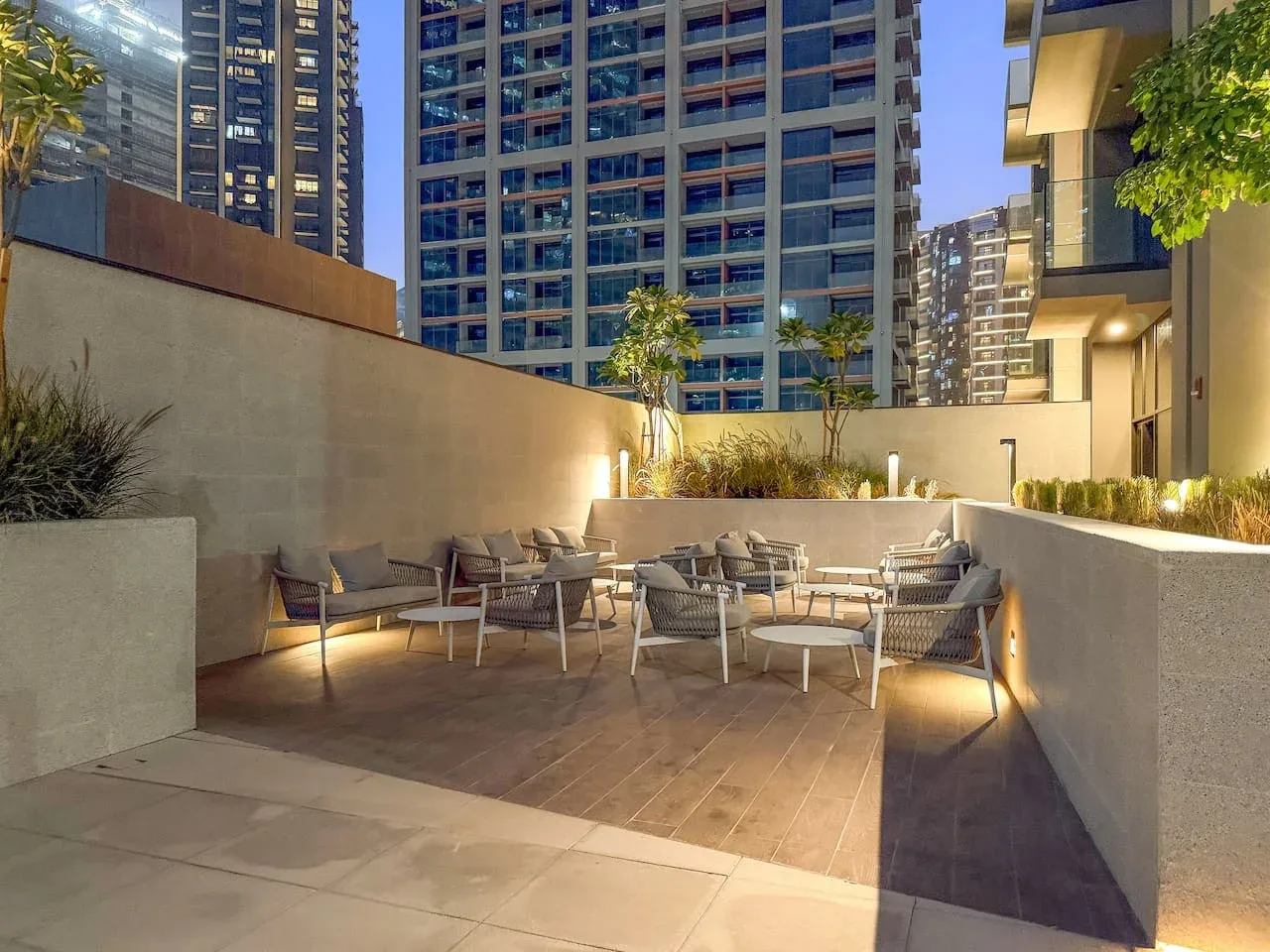 An outdoor seating area with tables and chairs among tall buildings at night.