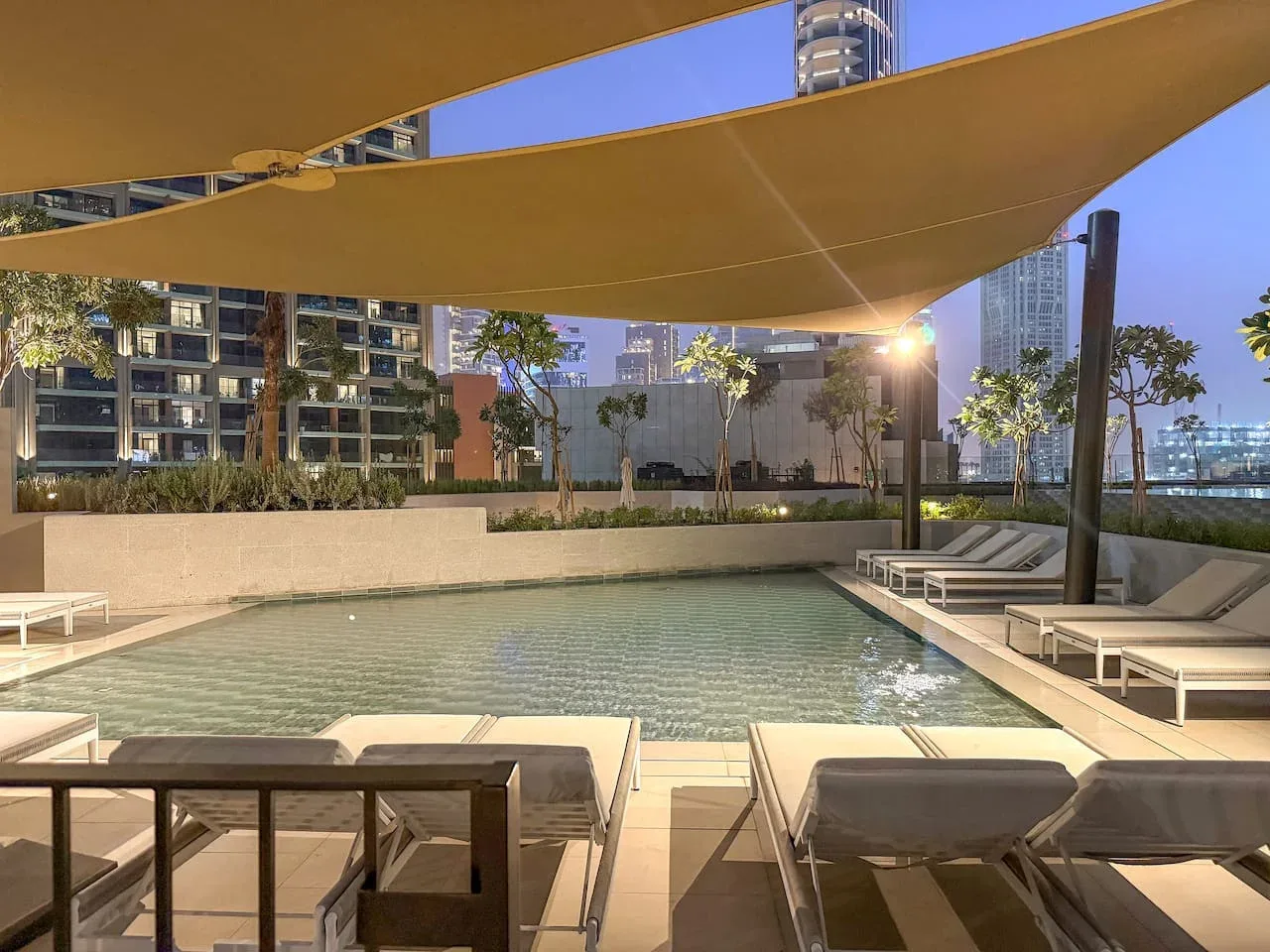 An outdoor swimming pool with lounge seating beneath a large shade canopy.